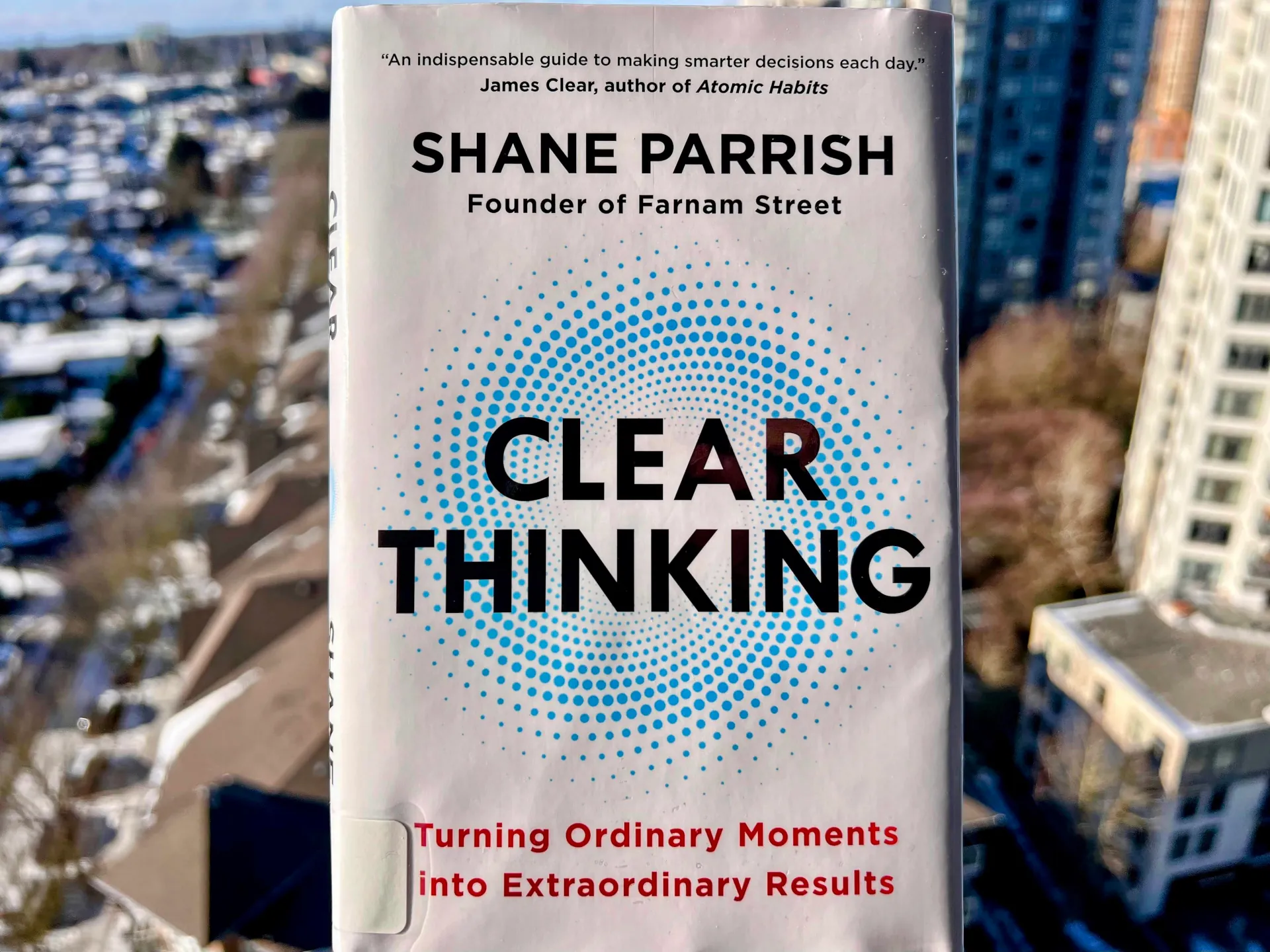 Cover of Clear Thinking by Shane Parrish held up against a blurred city skyline